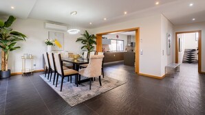 Un comedor moderno con suelo de madera oscura, una mesa central con sillas y plantas en macetas.