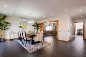 A modern dining area with a dark wood floor, a central dining table with chairs, and potted plants.