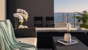 Un balcón con muebles de mimbre, una orquídea blanca y vista al mar.