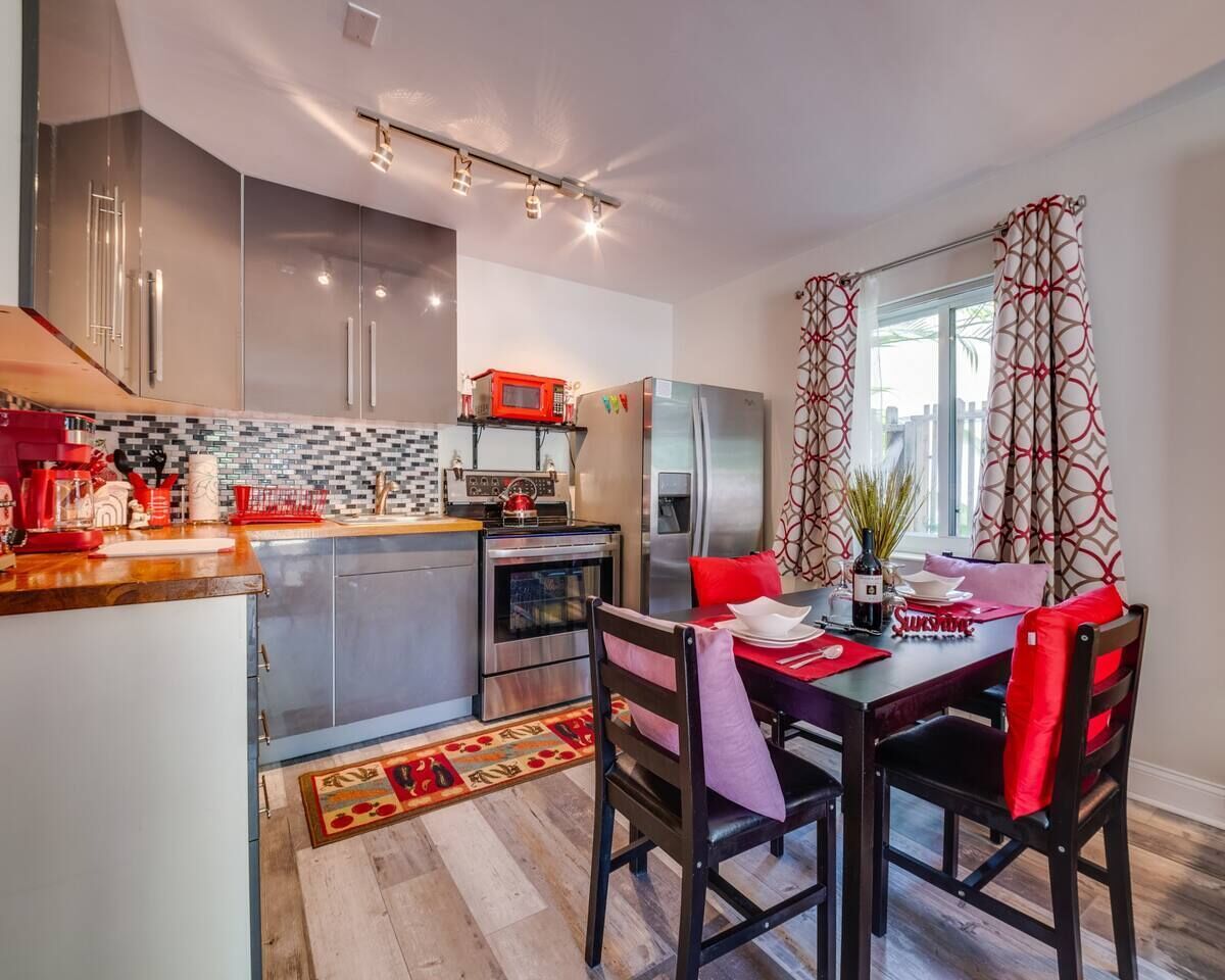 A modern kitchen with stainless steel appliances, a dining area with red chairs, and a patterned rug.