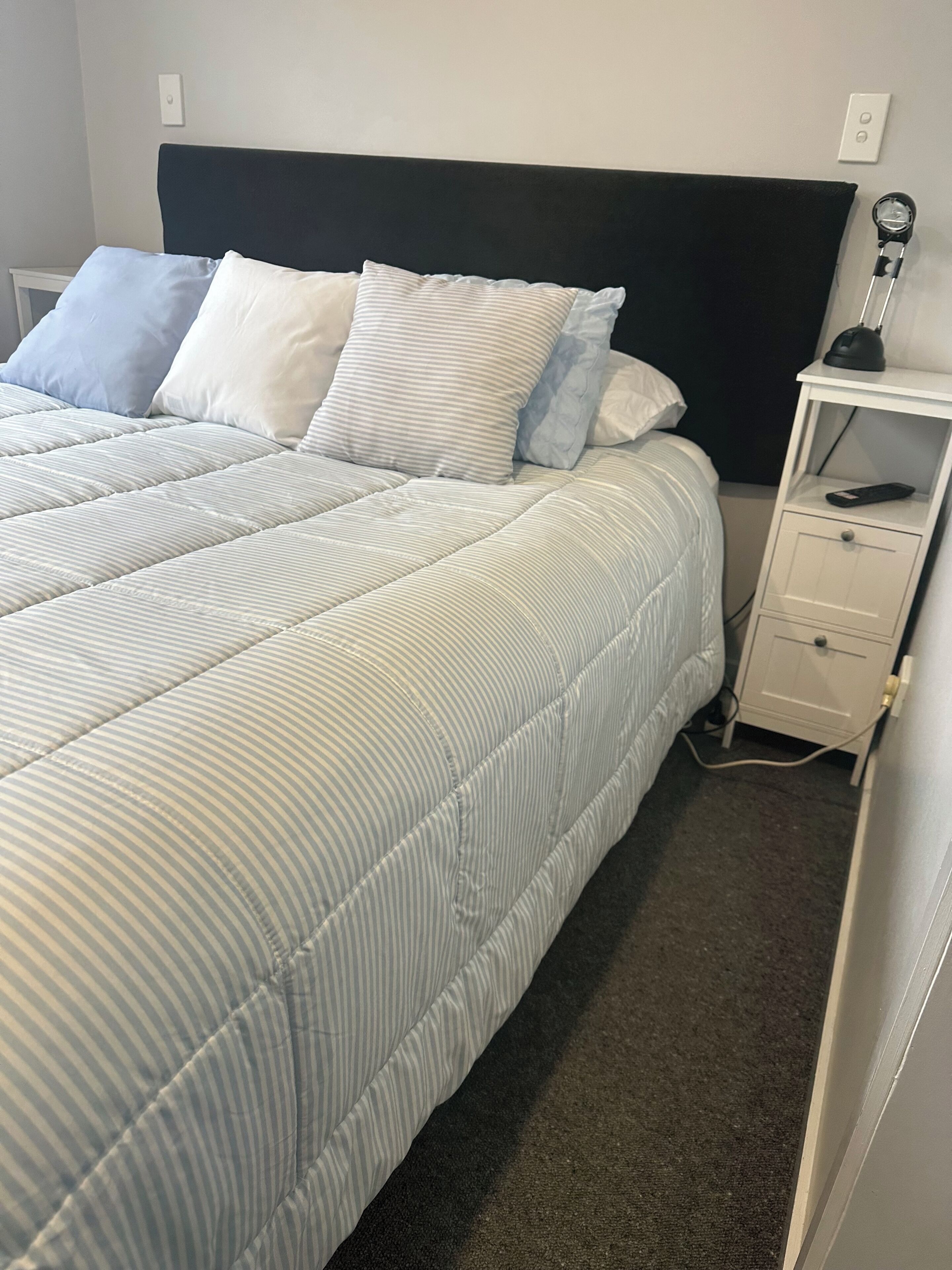Un lit avec une couette à rayures, une tête de lit noire et une table de chevet avec une lampe et une télécommande.