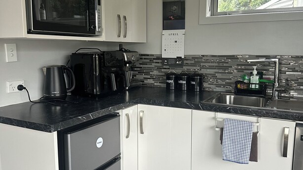 A modern kitchen with white cabinets, a black countertop, a microwave, a coffee machine, and a sink. - Modern Bach with a Rural view (Riverton)