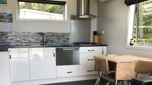 A modern kitchen with white cabinetry, a gas stove, and a dishwasher. There is a window with a view of greenery outside. - Modern Bach with a Rural view (Riverton)