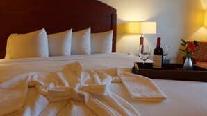 Cama bem arrumada com lençóis brancos, uma garrafa de vinho, um copo e uma bandeja com um vaso de flores.