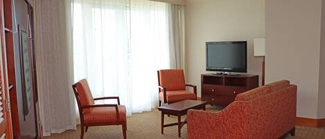 Habitación de hotel con sofá, dos sillones, una mesita de centro, televisor y mueble.