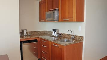 Una cocina compacta con armarios de madera, un microondas de acero inoxidable, una cafetera y un lavavajillas.