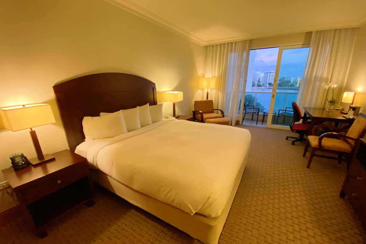 Habitación de hotel con una cama grande, dos mesitas de noche con lámparas, un escritorio con silla y vistas a la ciudad desde la ventana.