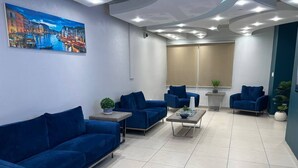 Uma área de espera moderna com sofás azuis, uma mesa de centro e uma pintura de uma paisagem urbana na parede.