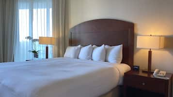 A hotel room with a large bed, a wooden headboard, two bedside tables with lamps, a small clock, and a vase with flowers.