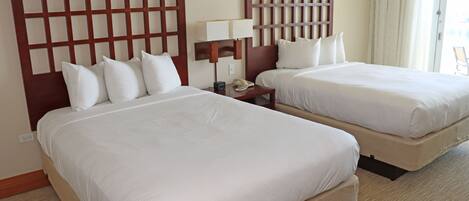 A hotel room with two beds, a nightstand with a lamp, and a telephone.