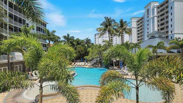 Un hotel con piscina rodeado de palmeras y sillas de descanso.