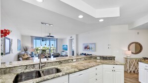 Una cocina moderna con armarios blancos, encimeras de granito y un lavamanos de acero inoxidable.
