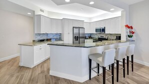 Una cocina moderna con armarios blancos, una isla central con taburetes altos, electrodomésticos de acero inoxidable y un salpicadero de azulejos.