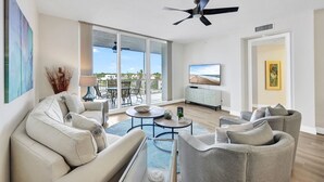 Amplia sala de estar con balcón, ventilador de techo, televisor de pantalla plana y un amplio ventanal con vistas a la playa.