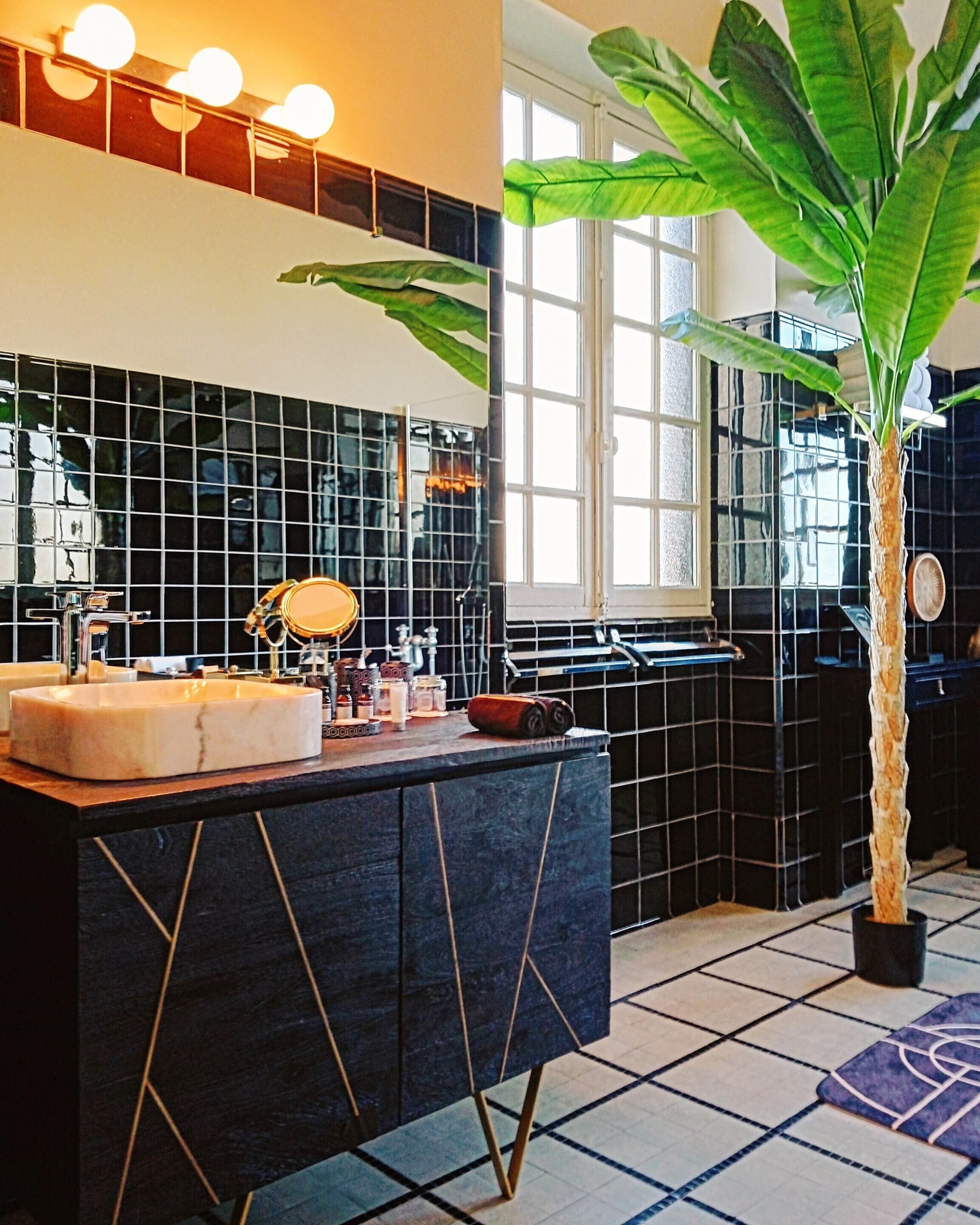 A modern bathroom with a black tiled backsplash, a large mirror, and a central sink.