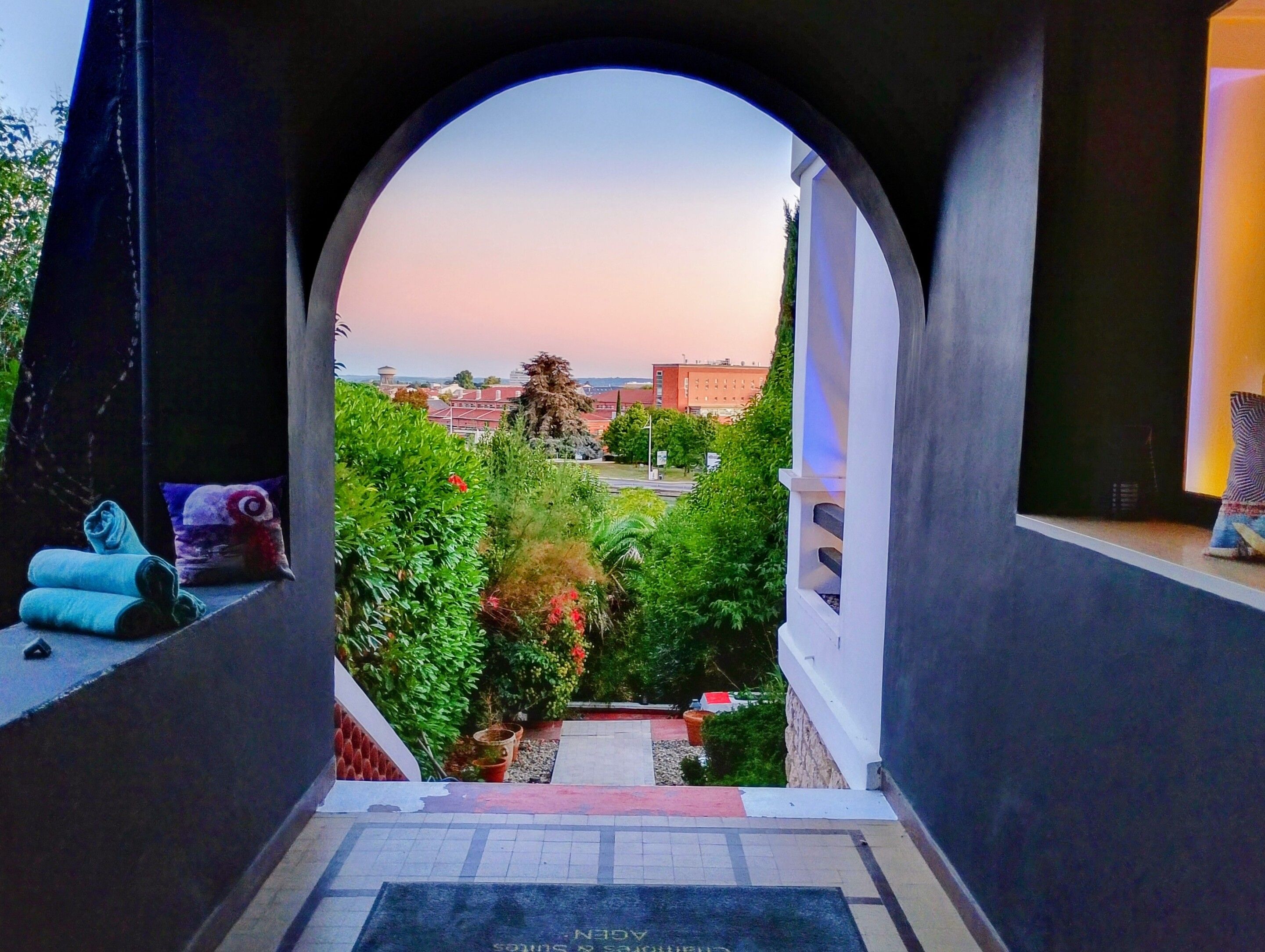 Blick durch einen Bogen auf einen Garten, einen Wasserturm und Gebäude im Hintergrund.