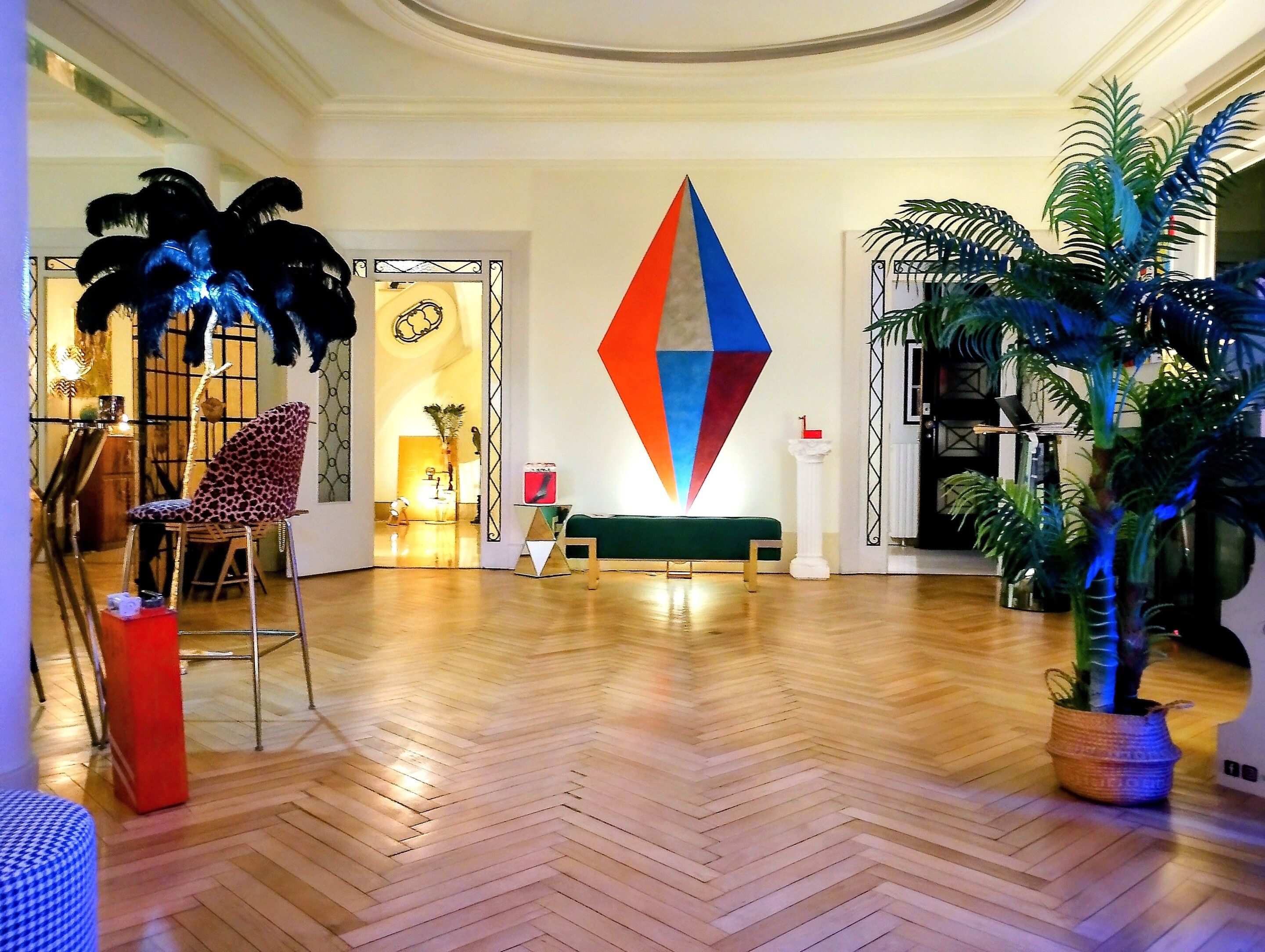 A spacious lobby with a herringbone wooden floor, a colorful geometric wall art piece, a leopard print chair, and a potted plant.