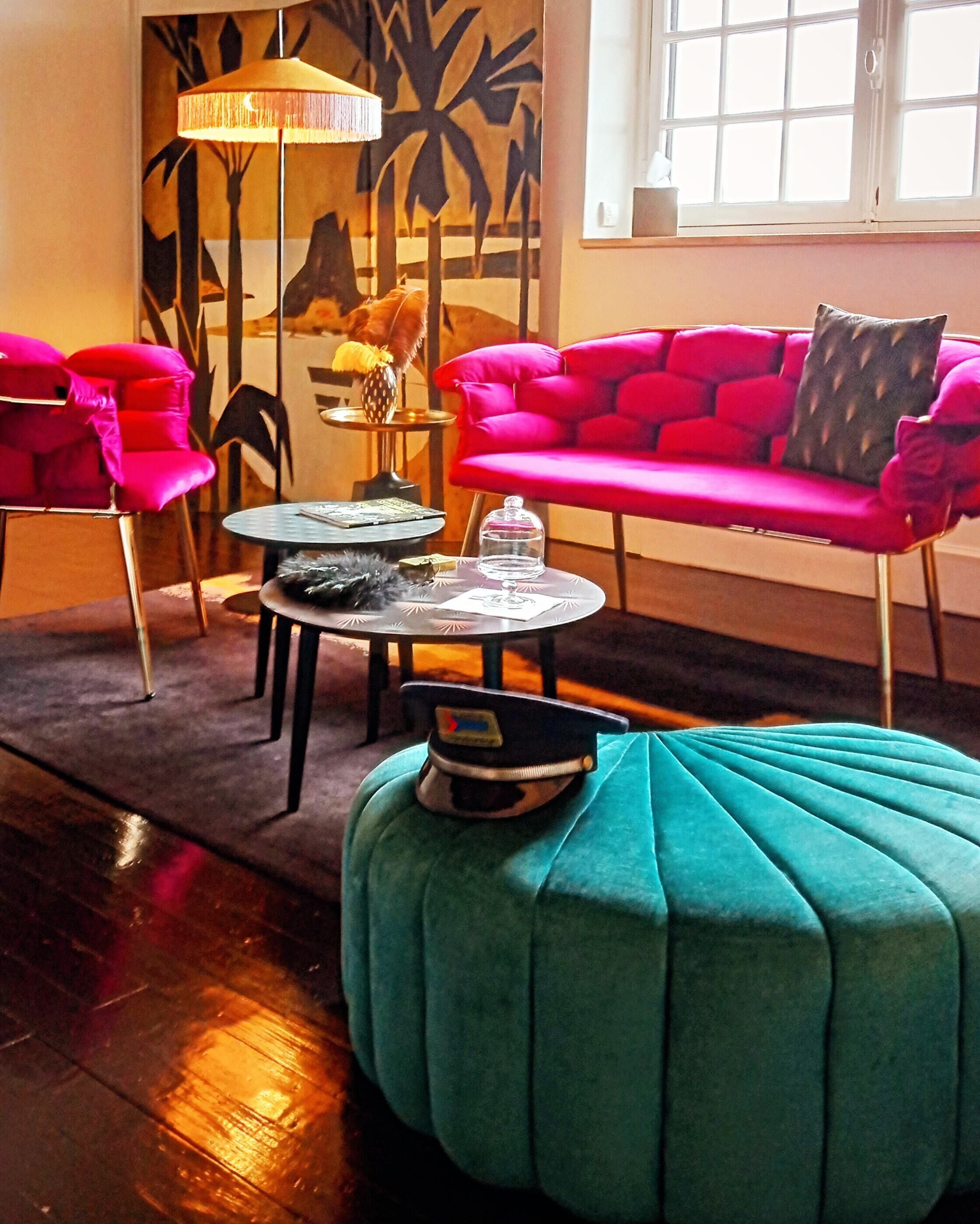 A room with a teal ottoman, a red sofa, and a black and white patterned wall.