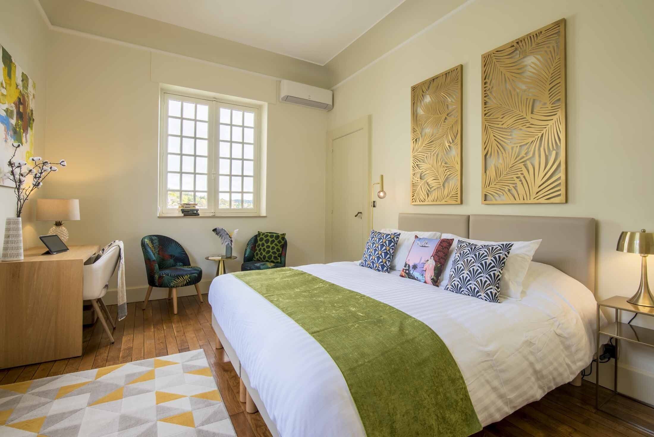 Habitación de hotel con una cama grande, un escritorio con una computadora portátil, dos sillas, un ventanal y decoración en la pared.