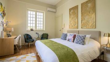 Habitación de hotel con una cama grande, un escritorio con una computadora portátil, dos sillas, un ventanal y decoración en la pared.
