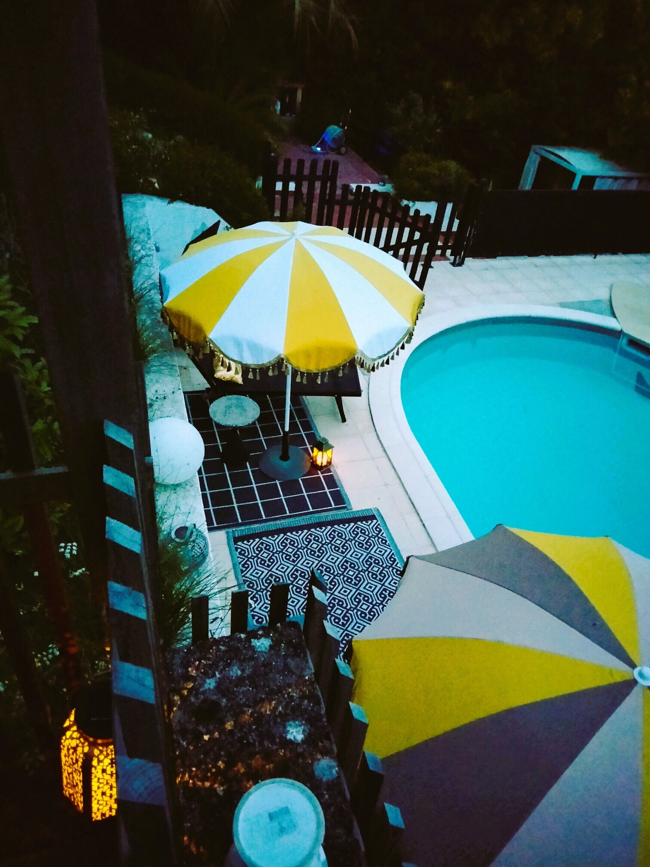 Zona de piscina con una sombrilla, una mesa y una silla.