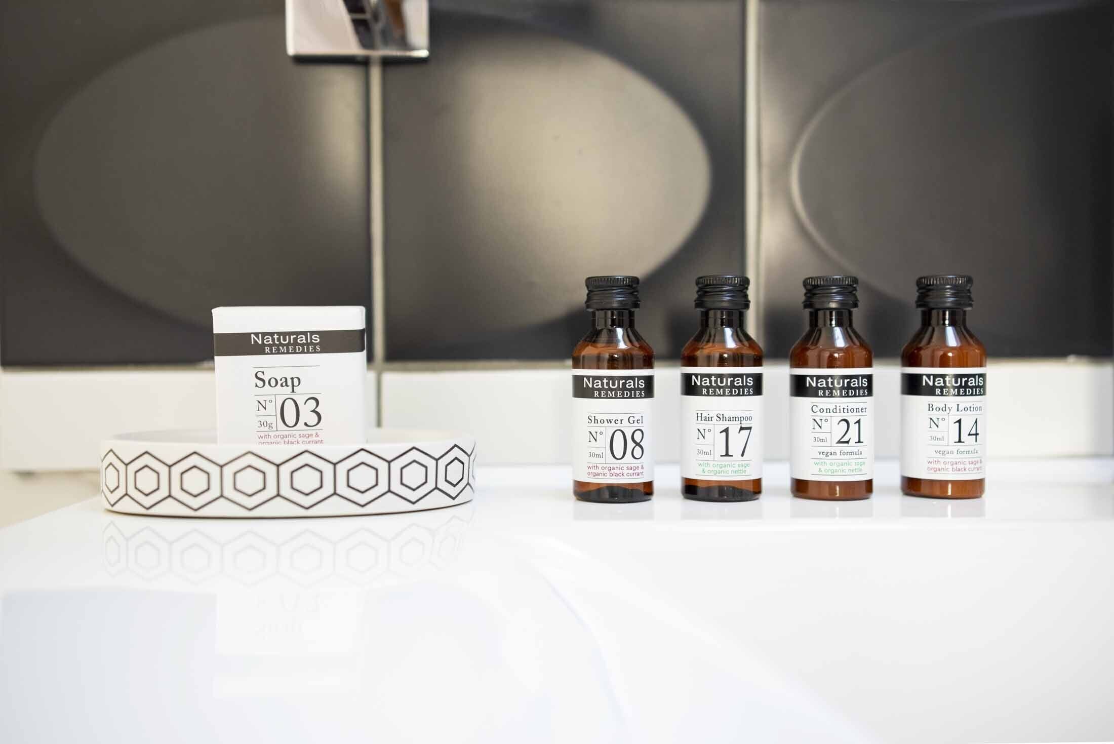 Exposição de produtos Naturals Remedies, incluindo sabonete, gel de banho, shampoo para cabelo, condicionador e loção corporal, sobre uma superfície branca.
