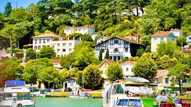 A marina with boats docked, surrounded by lush greenery and residential buildings. - Quand la Ville Dort (Agen)