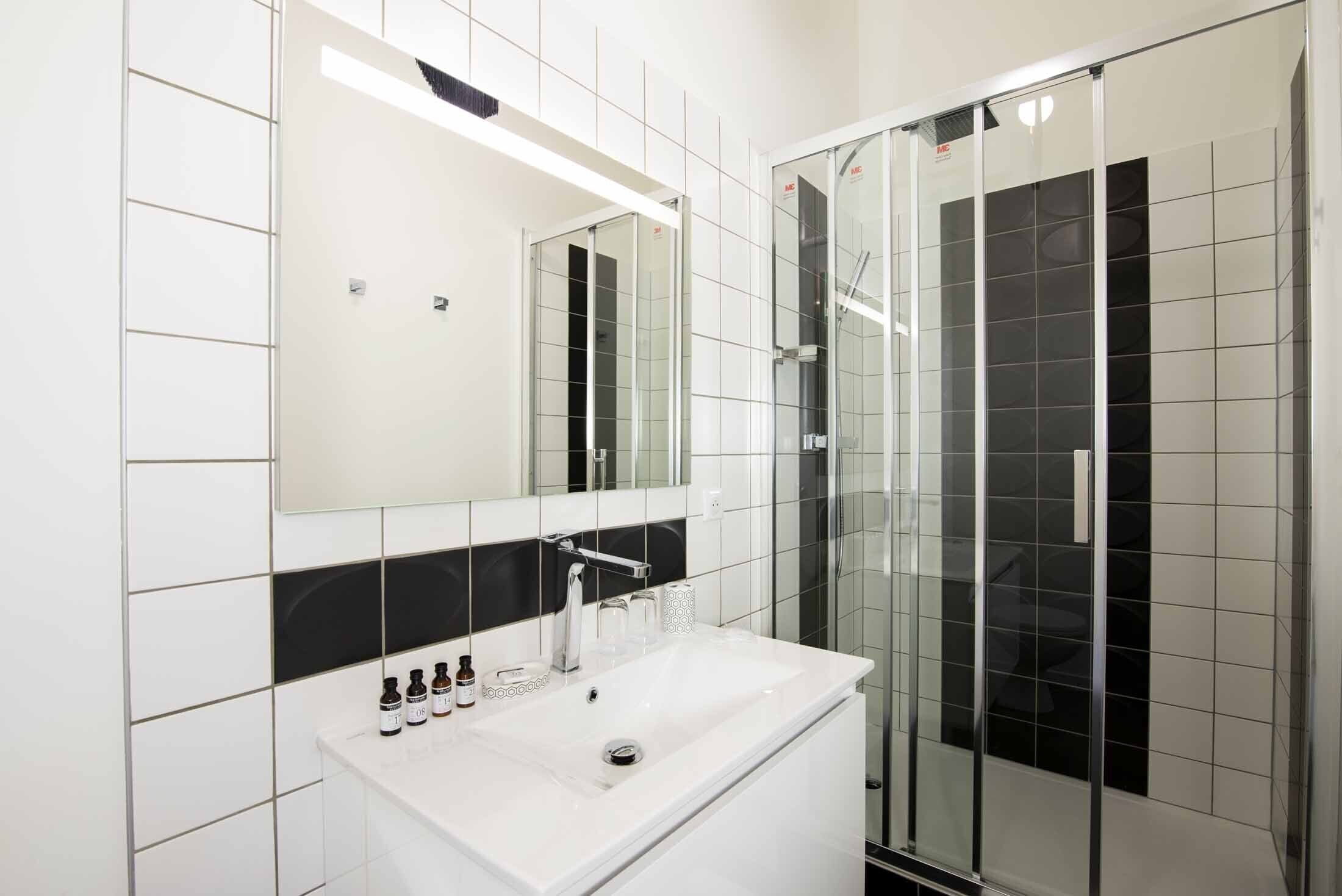 Une salle de bain moderne avec un lavabo blanc, un miroir et une cabine de douche en verre.