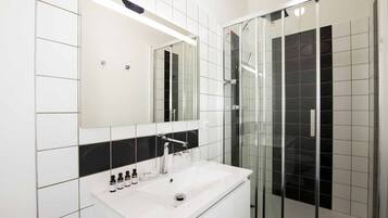 Un baño moderno con lavamanos blanco, espejo y cabina de ducha de vidrio.