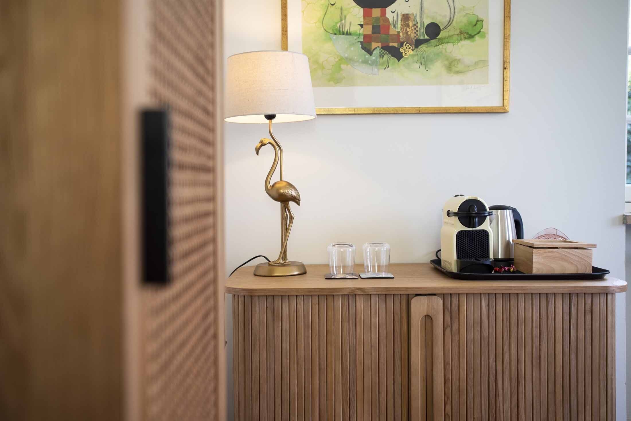 A wooden cabinet with a lamp, glasses, a coffee maker, and a tray with a box.