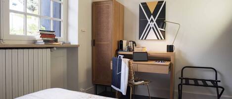 Une chambre à coucher avec un lit, un bureau avec un ordinateur portable, une chaise, une armoire et une fenêtre dont l’encadrement est garni de livres.