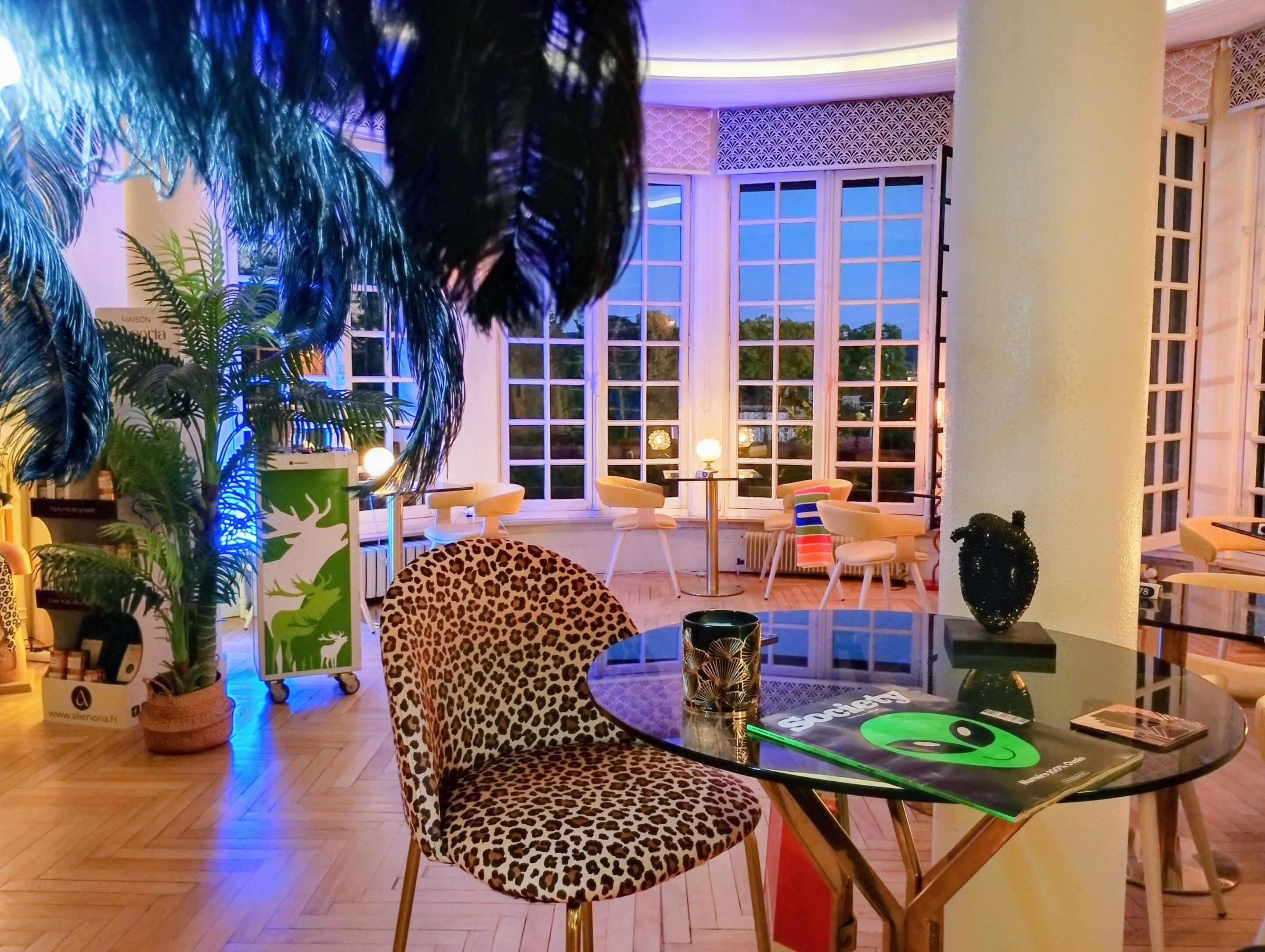 A modern interior with a glass table, a leopard print chair, and a view of the outdoors through large windows.