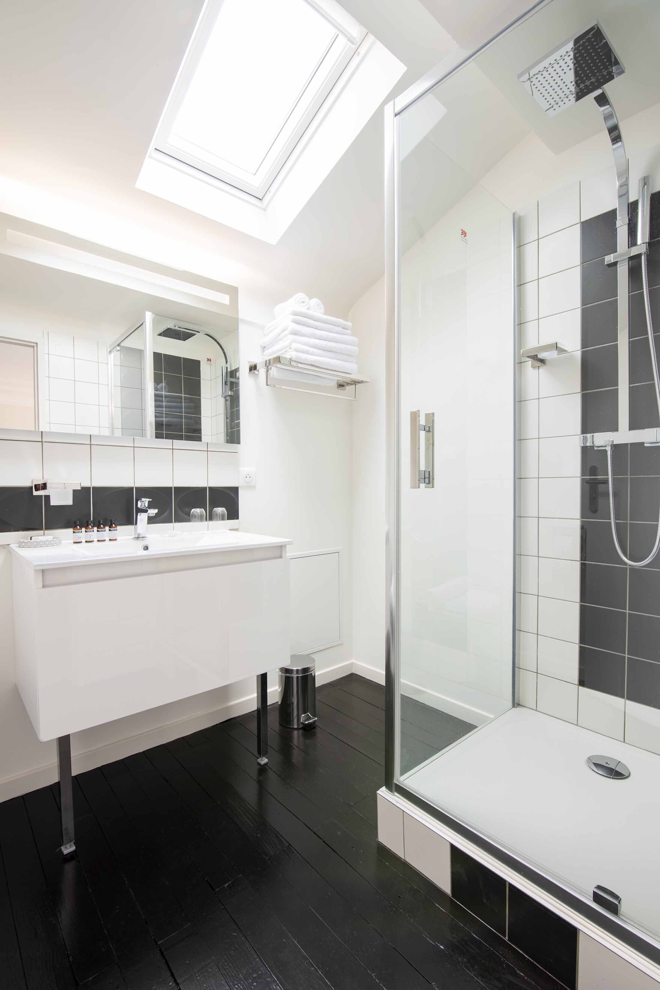 Un baño moderno con tragaluz, ducha con mampara de vidrio y tocador blanco.