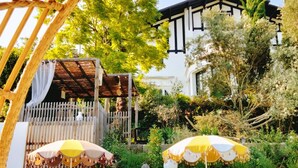 A pool area with lounge chairs and umbrellas, a pergola, and a white building with black trim in the background. - Quand la Ville Dort (Agen)