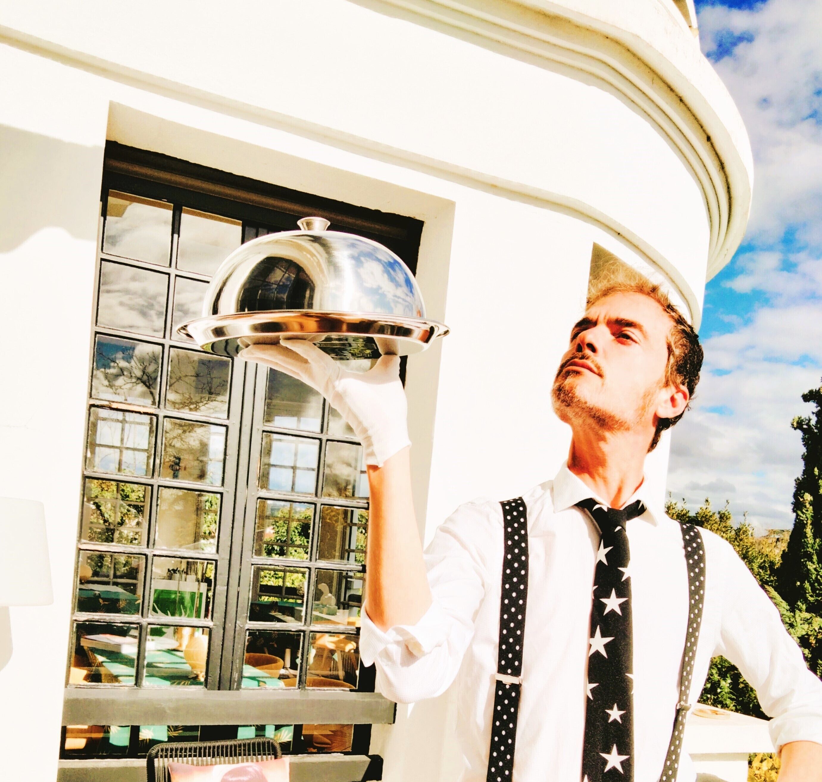 A person in a white shirt and black tie with stars, holding a silver tray.