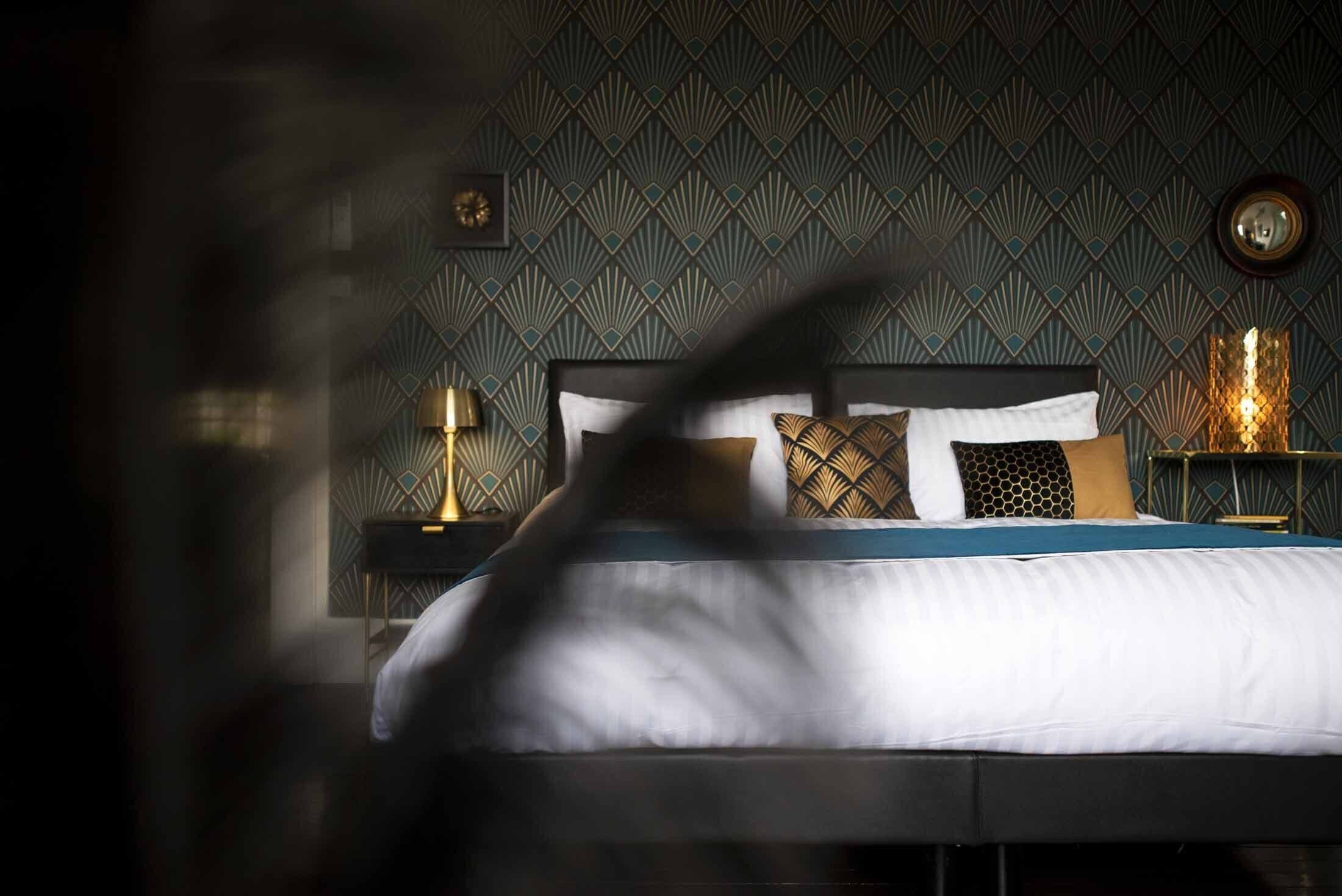 A bedroom with a patterned wallpaper, a bed with white bedding, and two bedside lamps.