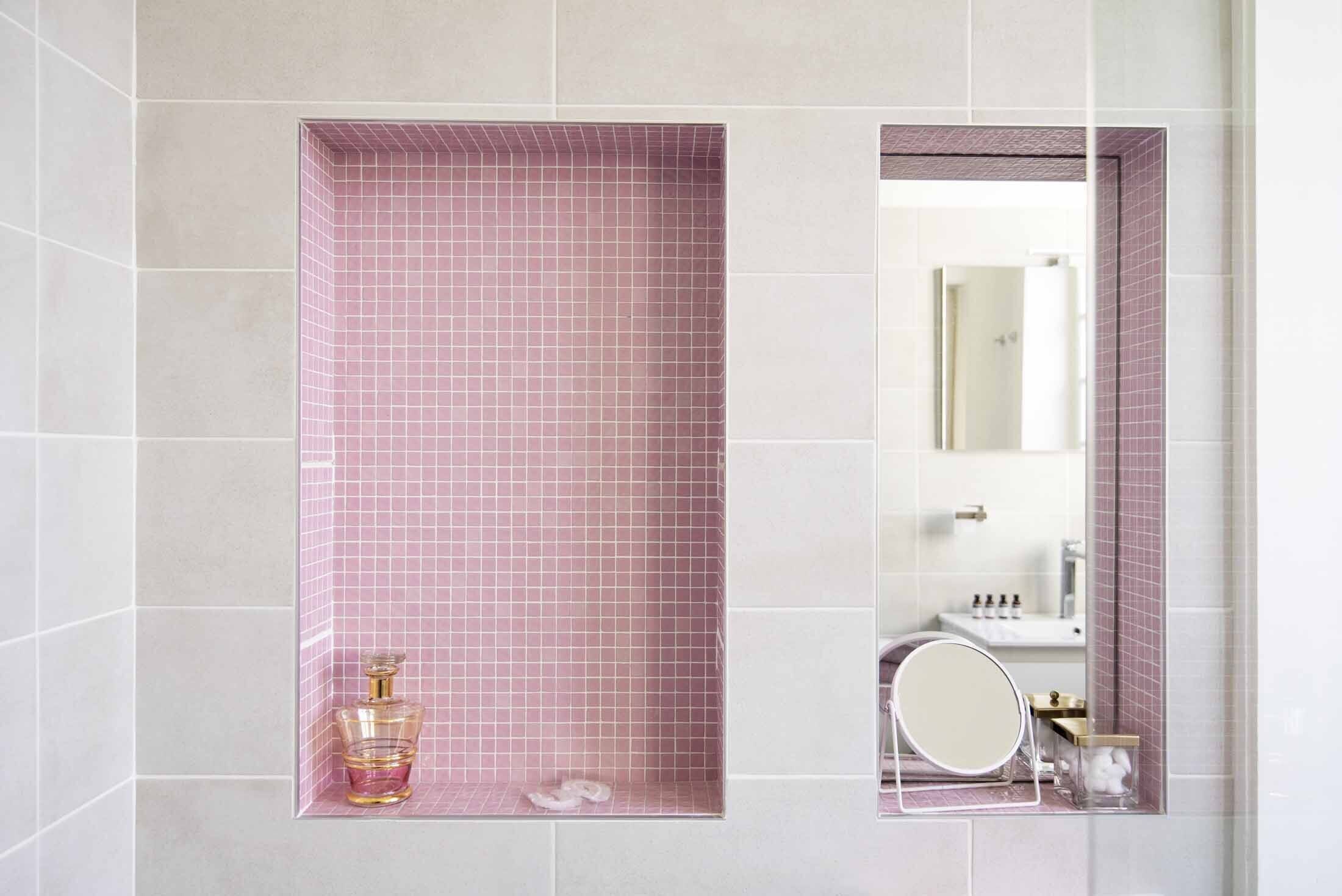 Un baño con cabina de ducha con azulejos rosas y un espejo sobre un lavabo.