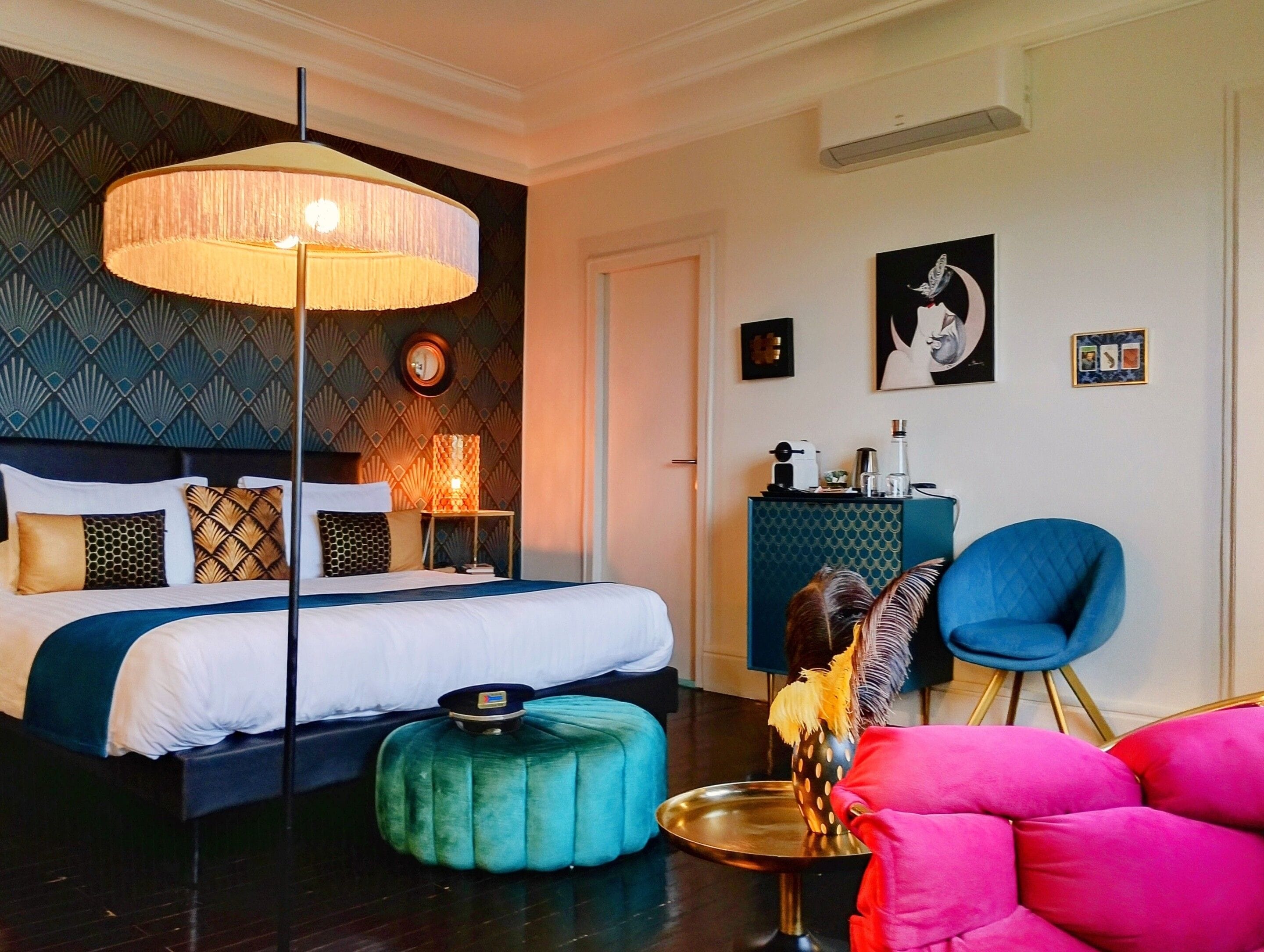 Une chambre d’hôtel moderne avec un grand lit, une table ronde, un fauteuil bleu et une lampe décorative.