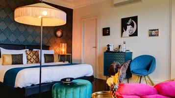 Une chambre d’hôtel moderne avec un grand lit, une table ronde, un fauteuil bleu et une lampe décorative.
