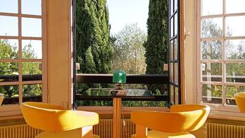 A room with a wooden floor, two yellow chairs, a small table, and large windows with a view of tall trees.
