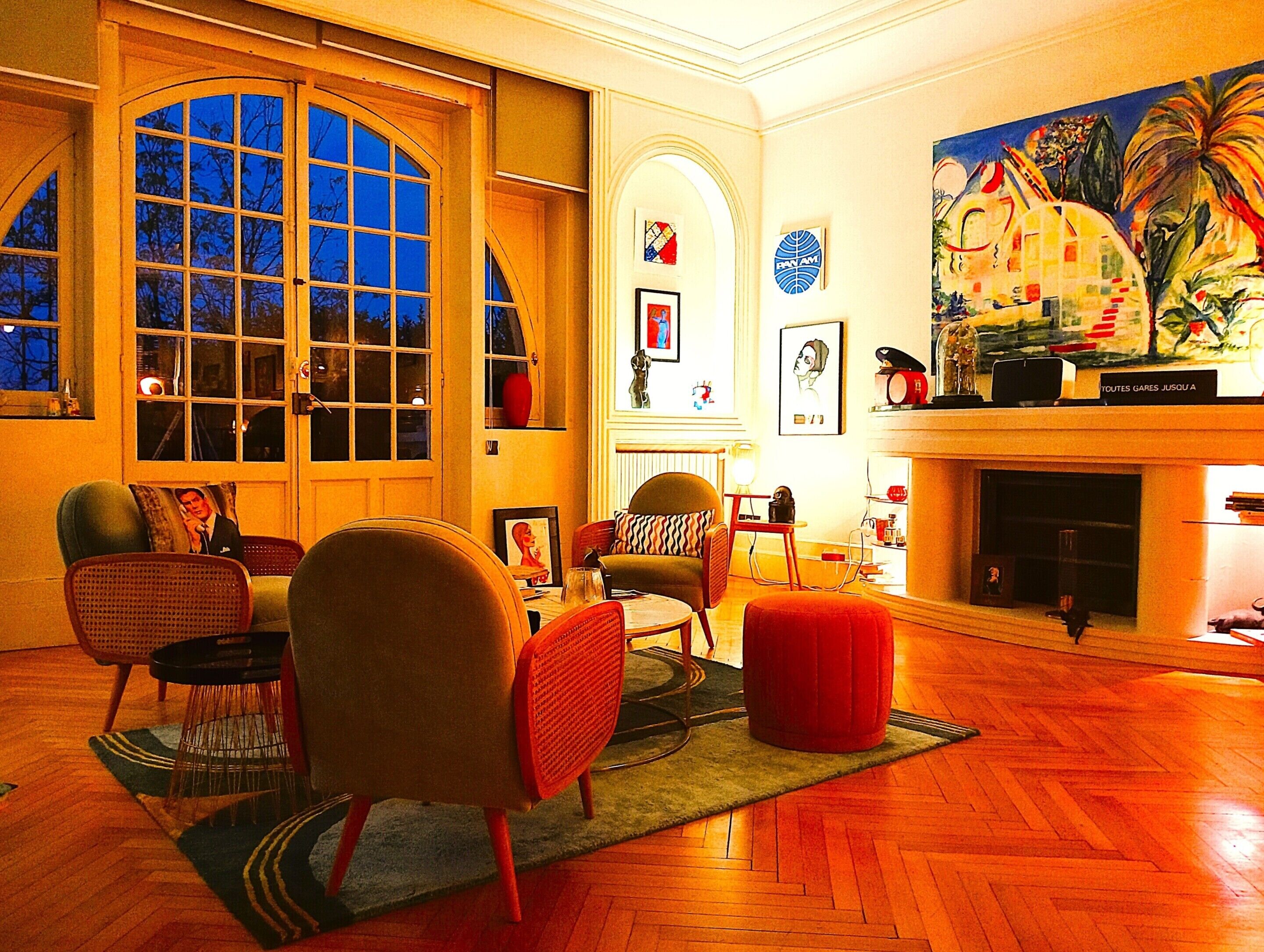A spacious living room with a large window, a fireplace, and various artworks.