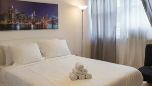 Un lit bien fait, avec des draps blancs et une pile de serviettes enroulées posée sur le lit.