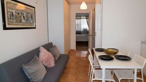 Un espace de vie compact avec un canapé gris, une table à manger entourée de chaises blanches et un tableau encadré accroché au mur.