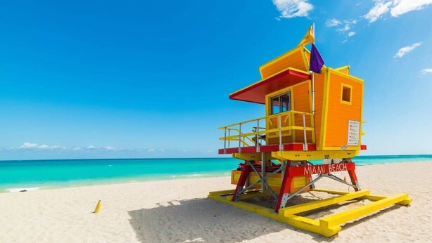 Une tour de surveillance sur une plage, avec une eau turquoise cristalline et un ciel d’un bleu éclatant.