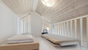 Een minimalistisch ingerichte slaapkamer met een groot bed, een kleiner bed en een stoel.
