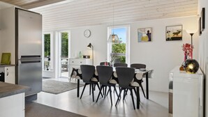 Een moderne keuken met een inbouwkoelkast, een eethoek met stoelen en een tafel, en grote ramen met uitzicht op de omgeving.