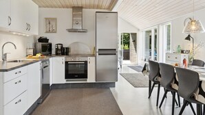 Een moderne keuken met witte kastjes, roestvrijstalen apparatuur en een eethoek met een tafel en stoelen.