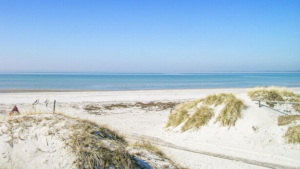 Een strand met zandduinen en een helder uitzicht over de oceaan.