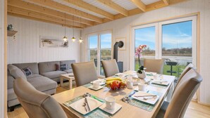 A dining area with a wooden table set for breakfast, a sofa, and large windows offering a view of the outdoors. - Gorgeous home in OstseeResort Olpenitz with sauna (OstseeResort Olpenitz)