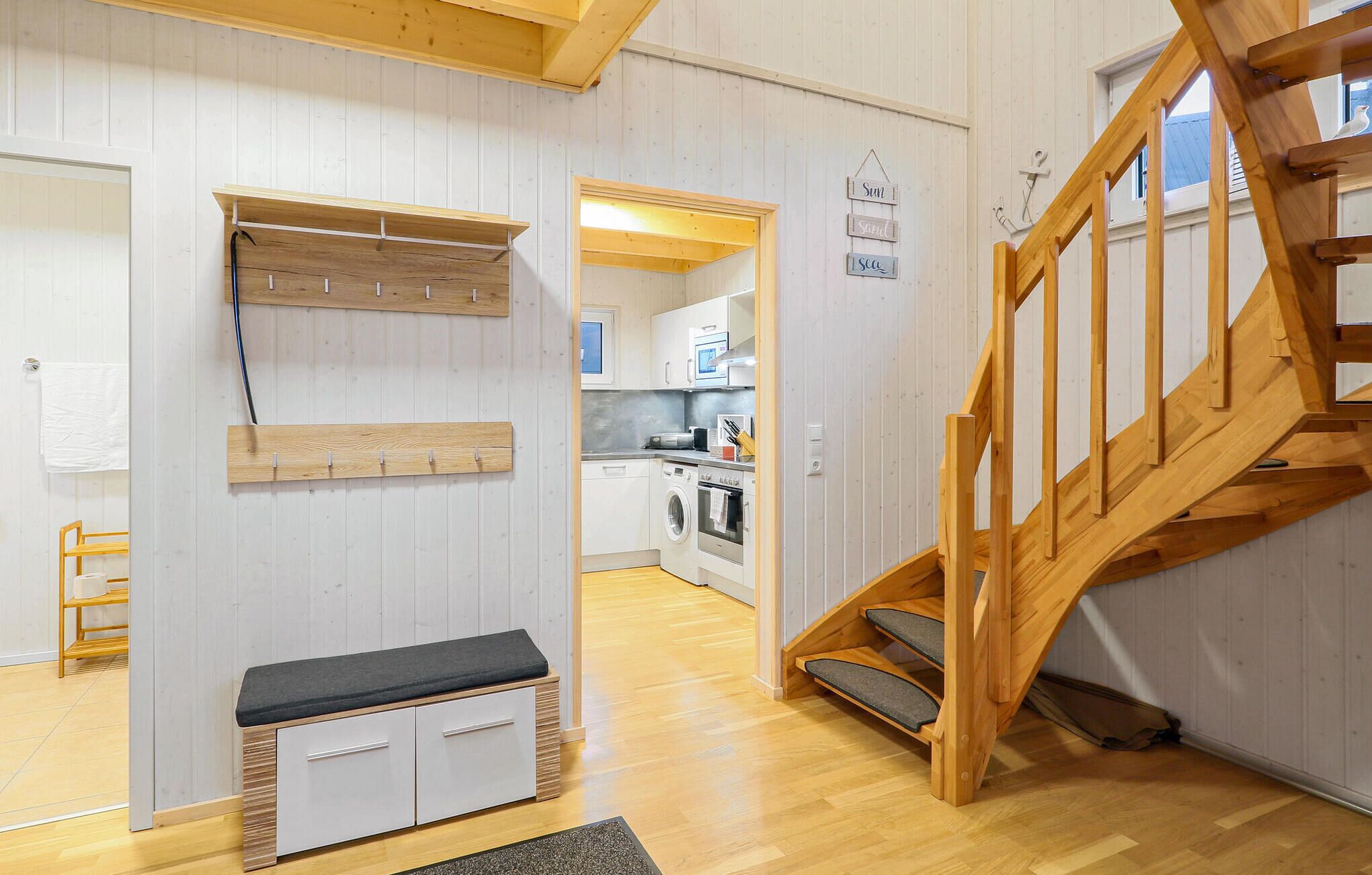 Una cocina moderna con armarios blancos, un banco de madera y una escalera con barandilla de madera.